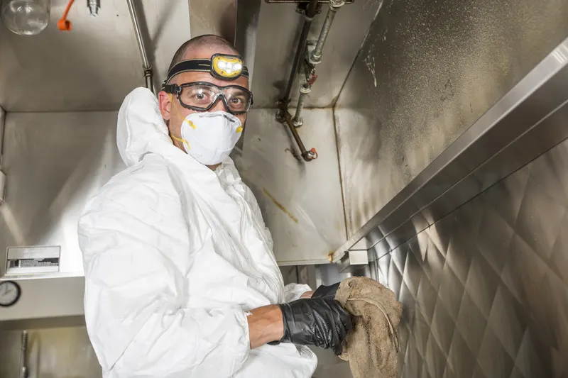Technician cleaning the filter slot and baffle track along the front of a kitchen exhaust hood